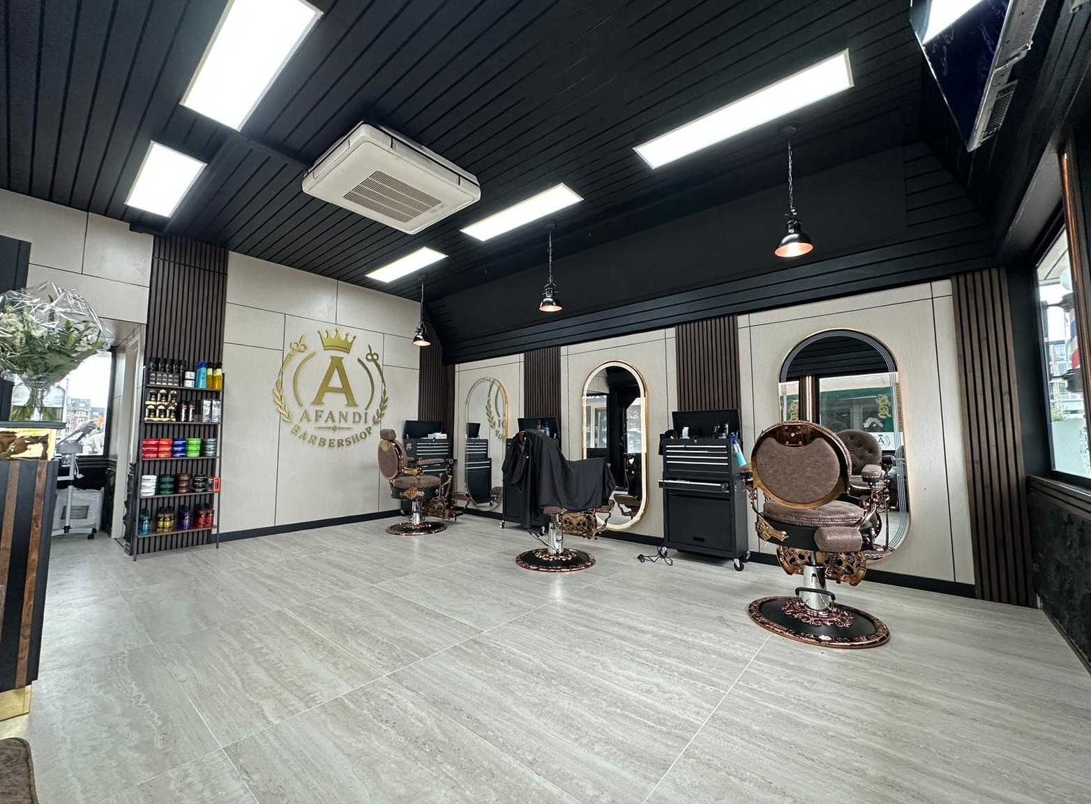 Interieur van Afandi barbershop: koperkleurige barberstoelen, boogspiegels, de donkere lattenplafond en het gouden bord aan de muur