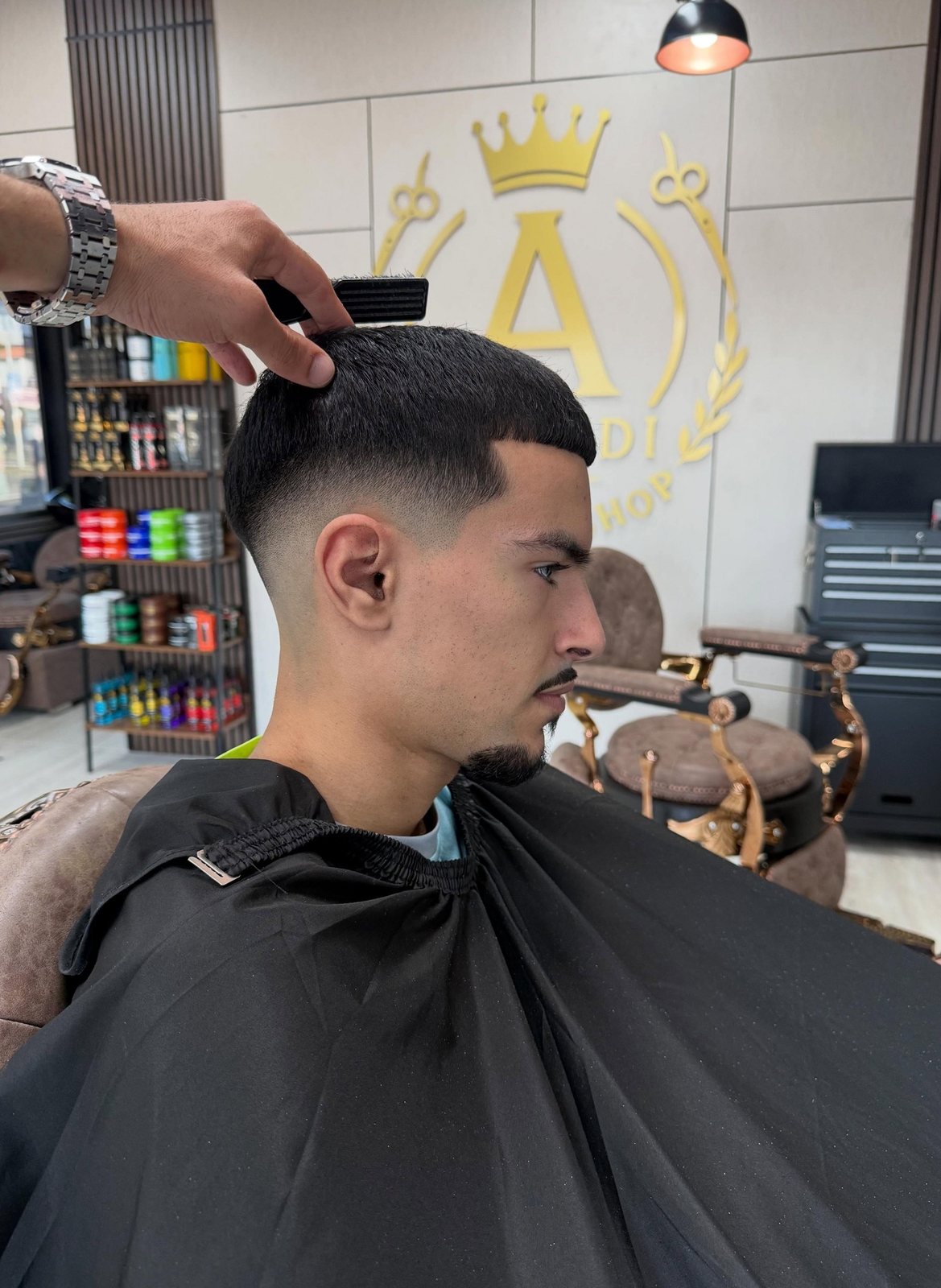 De barber werkt met kam en tondeuse een fade bij, met de productplank op de achtergrond
